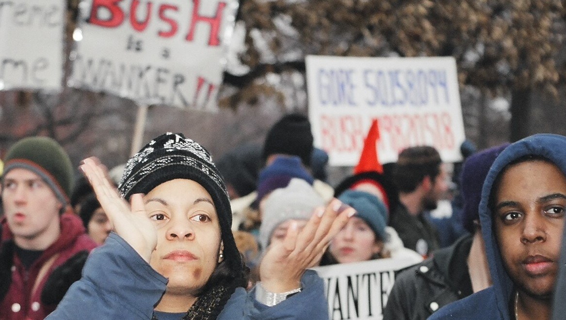 A protest at Stanton Park, Washington, D.C., on January 20, 2001, opposing Bush’s inauguration; the signs are participants’ claims.