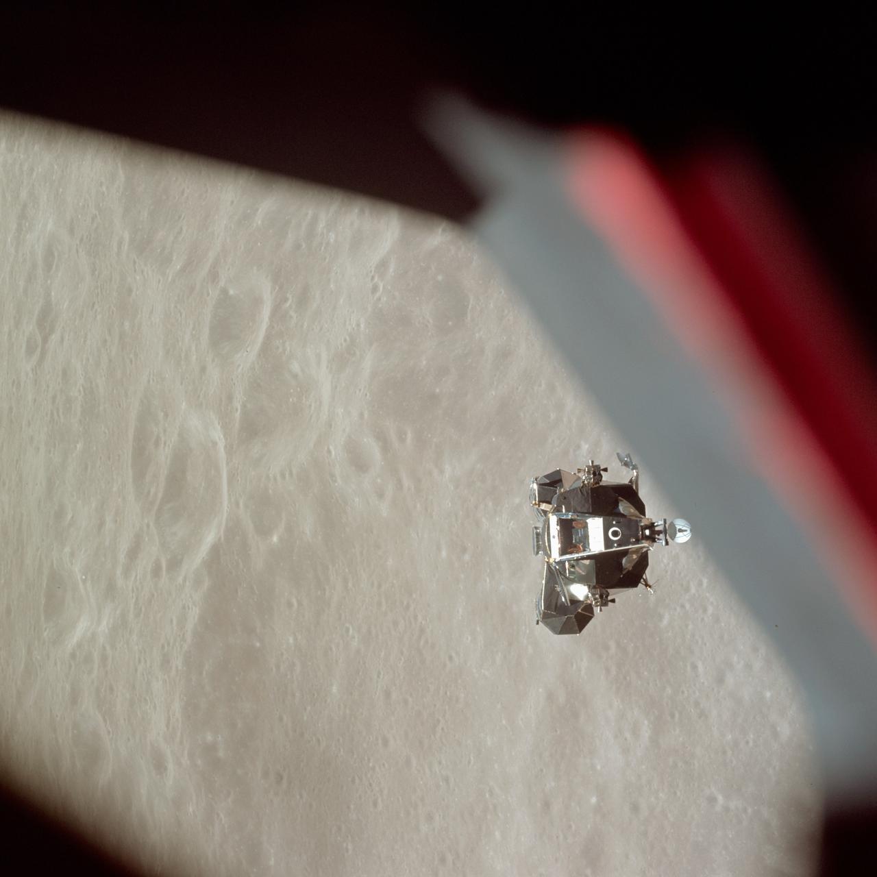 Topic photograph: The ascent stage of the Apollo 10 Lunar Module (LM) is photographed from the Command Module prior to docking in lunar orbit. The LM is approaching the Command and Service Modules from below. The LM descent stage had already been jettisoned. The lunar surface in the background is near, but beyond the eastern limb of the moon as viewed from Earth (about 120 degrees east longitude). The red/blue diagonal line is the spacecraft window.